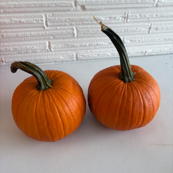 Two small orange pumpkins on a white surface