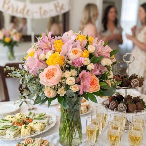 Pink and yellow floral centerpiece in a glass vase on a banquet table