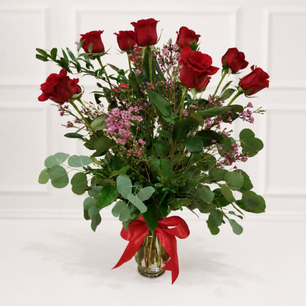 Red roses in a glass vase with pink filler flowers and a red ribbon
