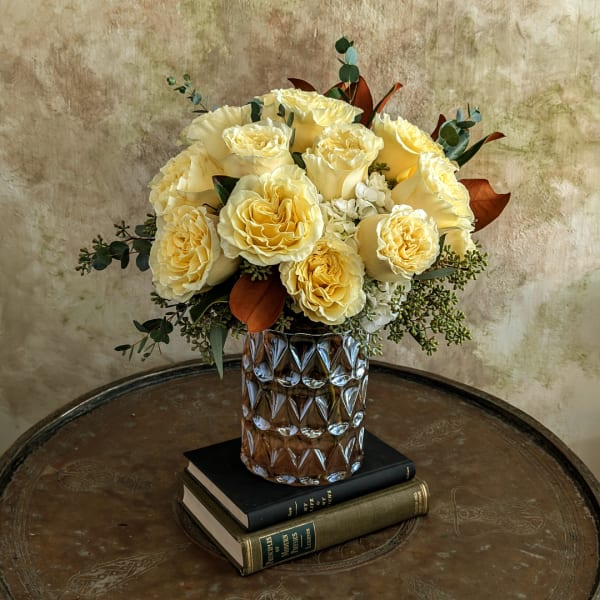 Yellow rose bouquet in a textured glass vase on stacked books