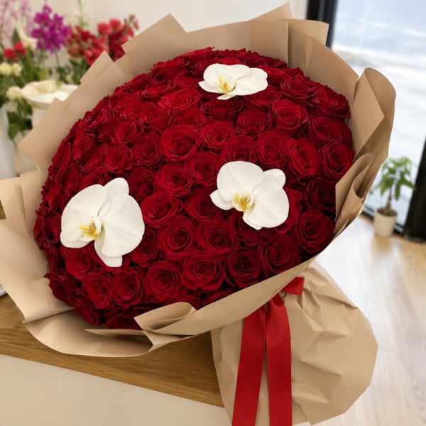 Large bouquet of red roses with white orchids wrapped in tan paper
