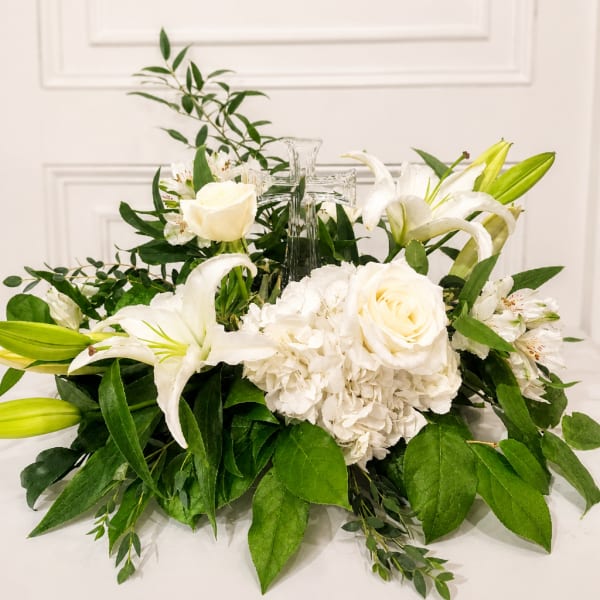 White floral arrangement with lilies, roses, and a clear glass cross