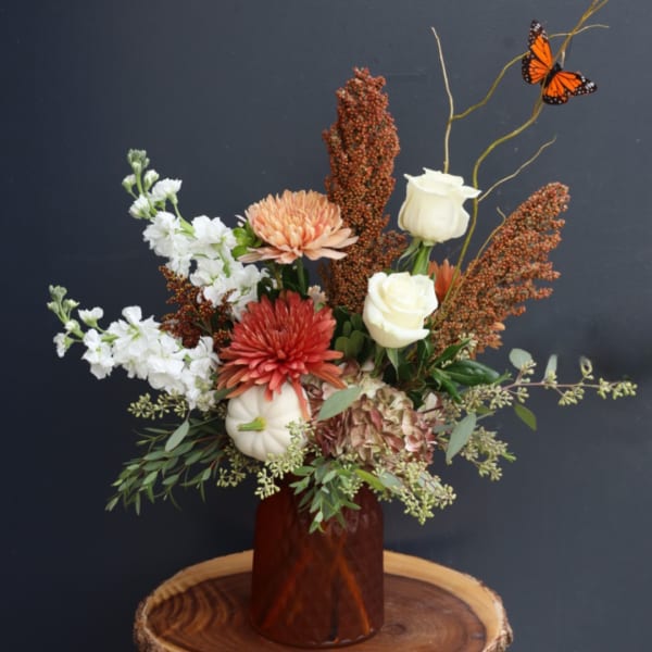 Autumn floral arrangement in a brown vase with white roses and orange blooms
