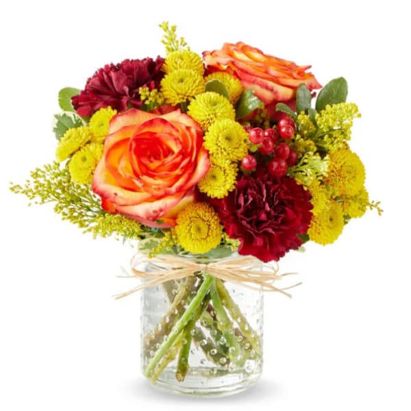 Mixed bouquet of orange roses and yellow and burgundy mums in a glass jar vase