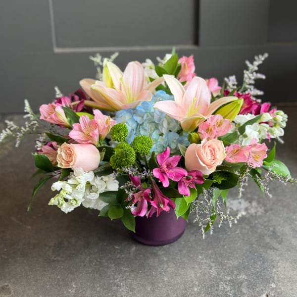 Mixed bouquet with lilies, roses, hydrangea, and pink flowers in a purple vase