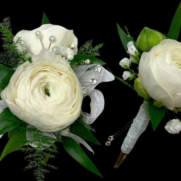 Two white floral boutonnieres with ribbon and pearl accents on a black background