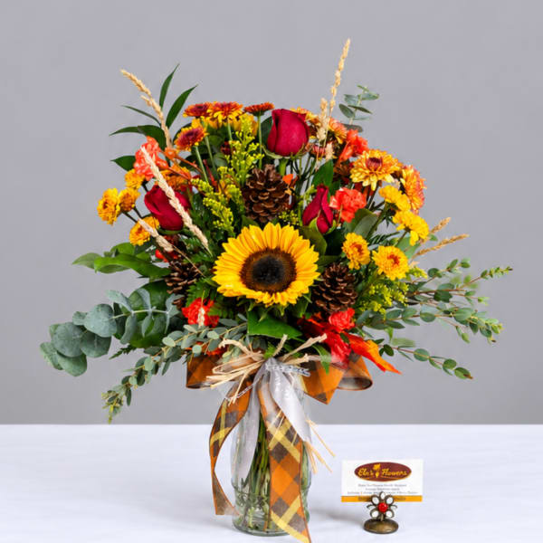 Autumn bouquet with sunflowers, red roses, and orange mums in a glass vase