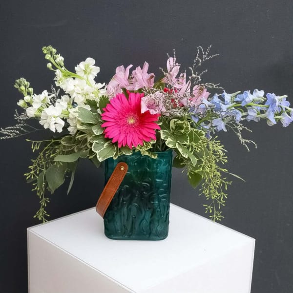 Mixed bouquet in a teal glass vase with a leather strap