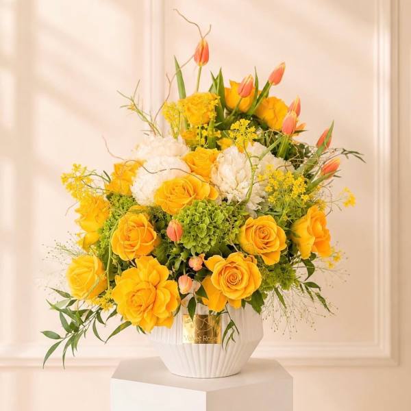 Yellow roses and white blooms in a white vase with pink tulips