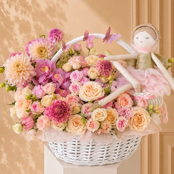 Pink and peach flowers in a white basket with a doll topper