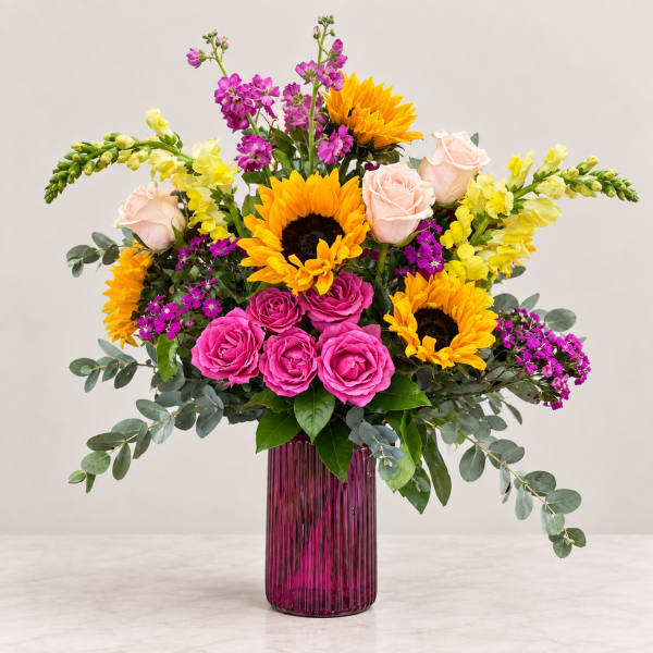 Bright mixed bouquet with sunflowers, pink roses, and yellow blooms in a purple vase