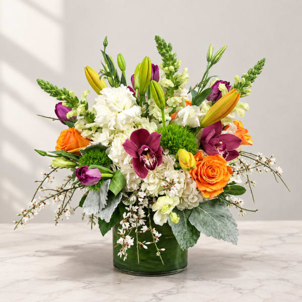 Colorful bouquet in a green glass vase with lilies, roses, orchids, and white blooms