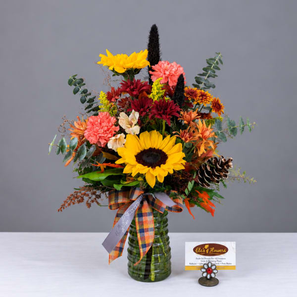 Mixed autumn bouquet in a green glass vase with a plaid ribbon