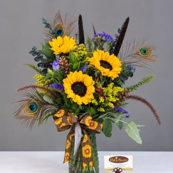 Sunflower bouquet in a green glass vase with peacock feathers and a ribbon