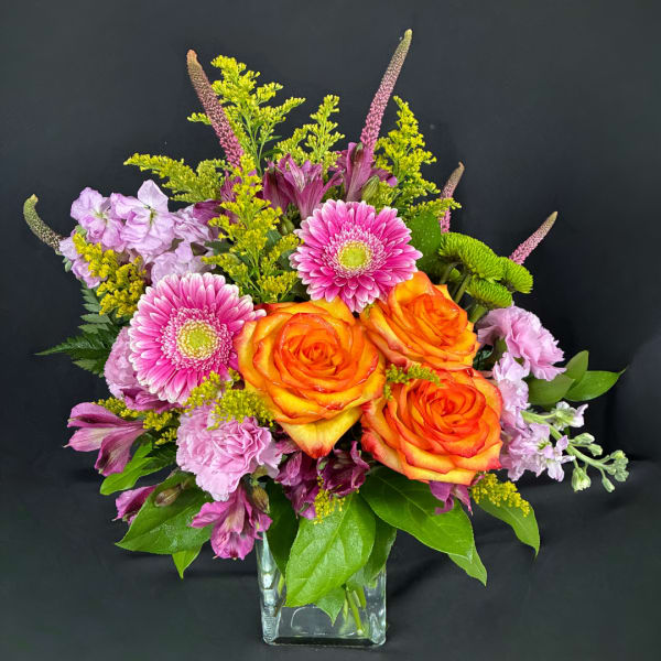 Orange roses and pink gerbera daisies in a clear square vase