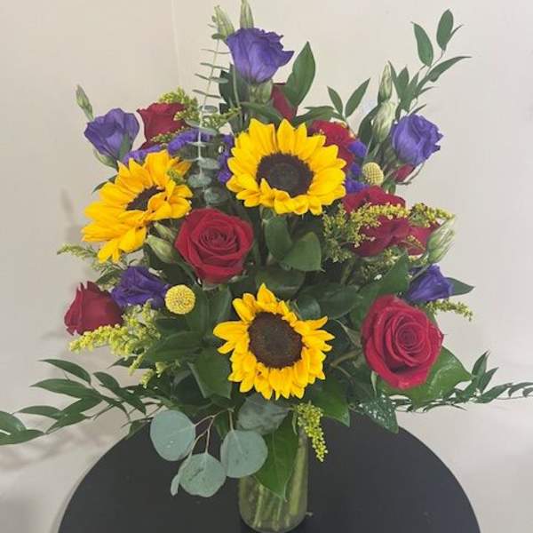 Bouquet of sunflowers, red roses, and purple blooms in a glass vase