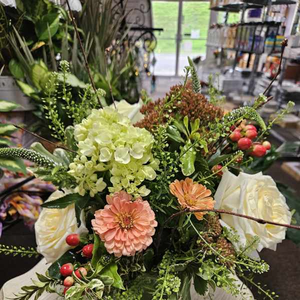 Low mixed arrangement with peach blooms, white roses, hydrangea, and berries in a square glass vase