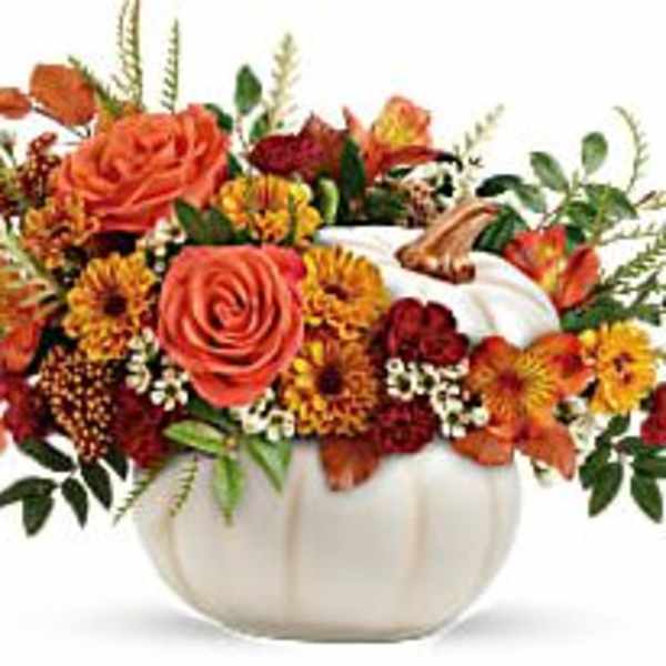 Orange and red floral arrangement in a white pumpkin vase