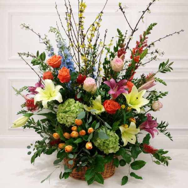 Large mixed flower arrangement in a wicker basket with lilies, roses, and branches