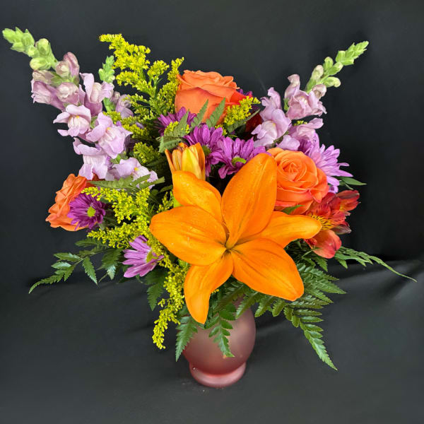 Colorful bouquet with orange lilies, roses, and purple flowers in a frosted vase