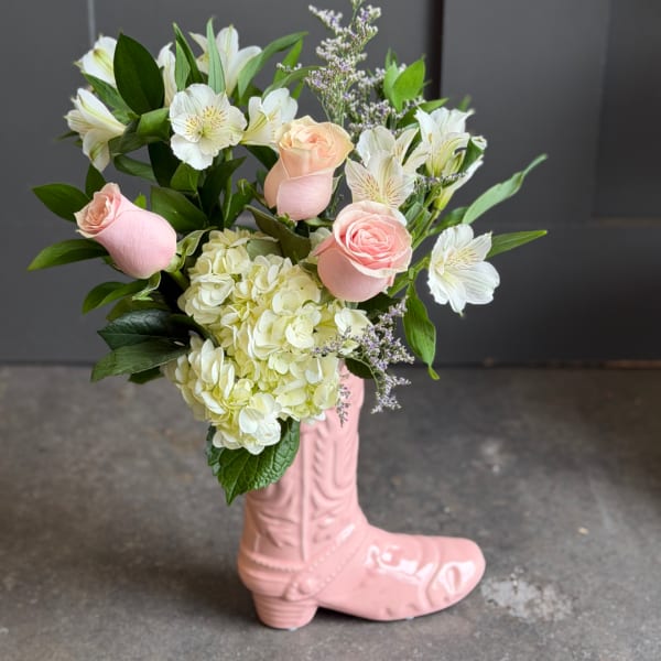 Pink roses and white flowers arranged in a pink boot vase