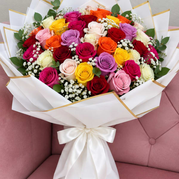 Bouquet of multicolored roses wrapped in white paper with a satin bow