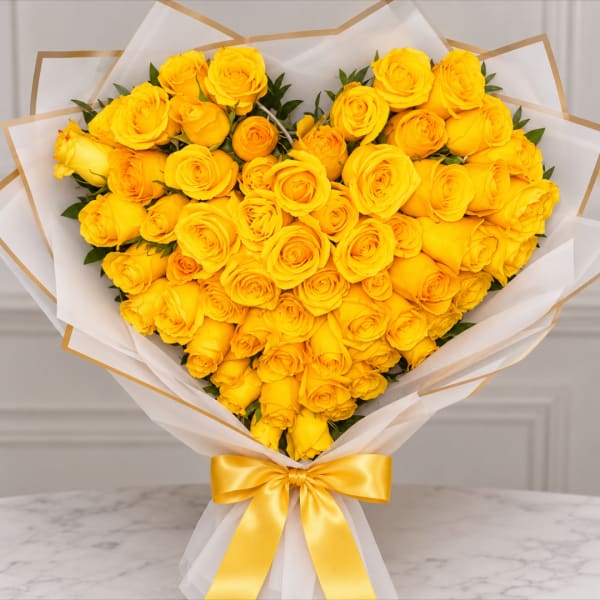 Heart-shaped bouquet of yellow roses wrapped in white paper with a gold ribbon