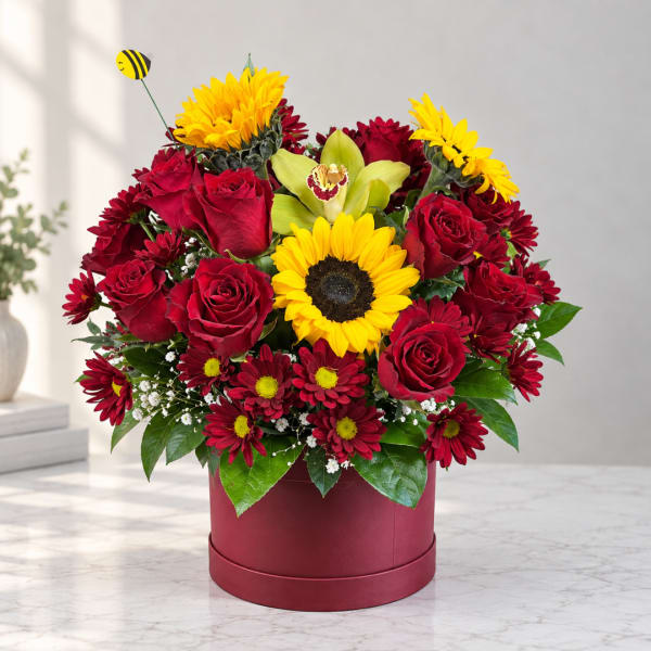 Red roses and yellow sunflowers in a burgundy box with a bee pick.