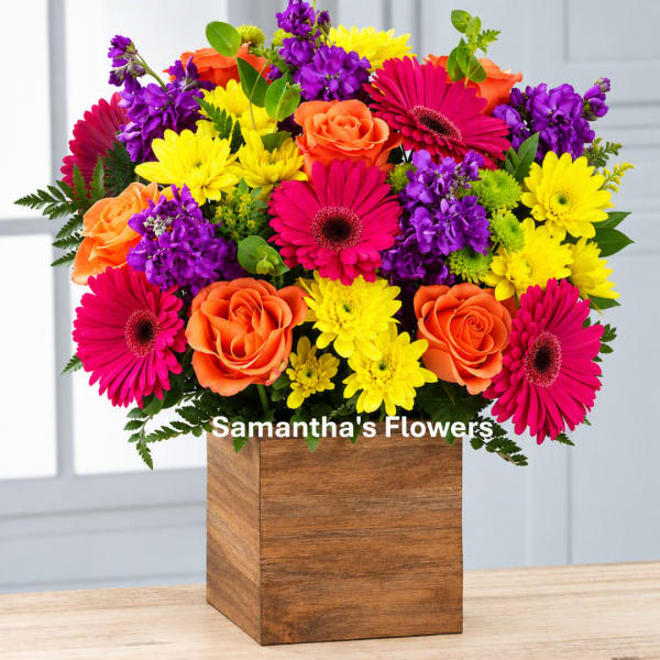 Bright mixed bouquet in a wooden cube vase with pink, orange, yellow, and purple flowers.