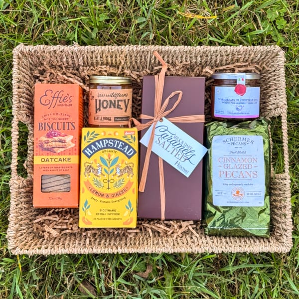 Gift basket with biscuits, honey, tea, chocolate, jam, and pecans on grass