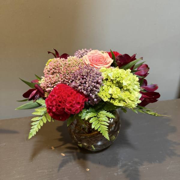 Mixed bouquet in a round glass vase with pink, red, and green blooms