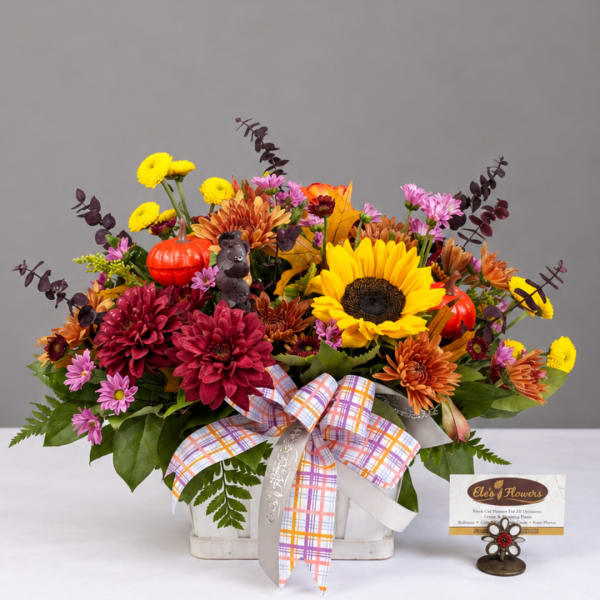 Autumn flower arrangement in a white basket with a plaid ribbon and small pumpkins