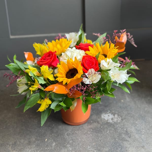 Bouquet of sunflowers, red roses, and white alstroemeria in an orange vase