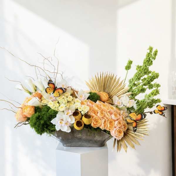 Large floral arrangement with peach roses, white orchids, and green accents in a gray vase