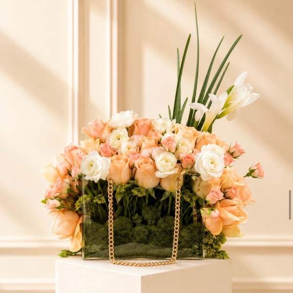 Peach and white rose arrangement in a clear rectangular vase with a gold chain handle