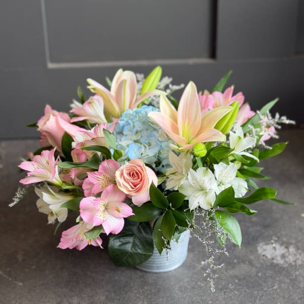 Pastel bouquet with lilies, roses, alstroemeria, and blue hydrangea in a white vase