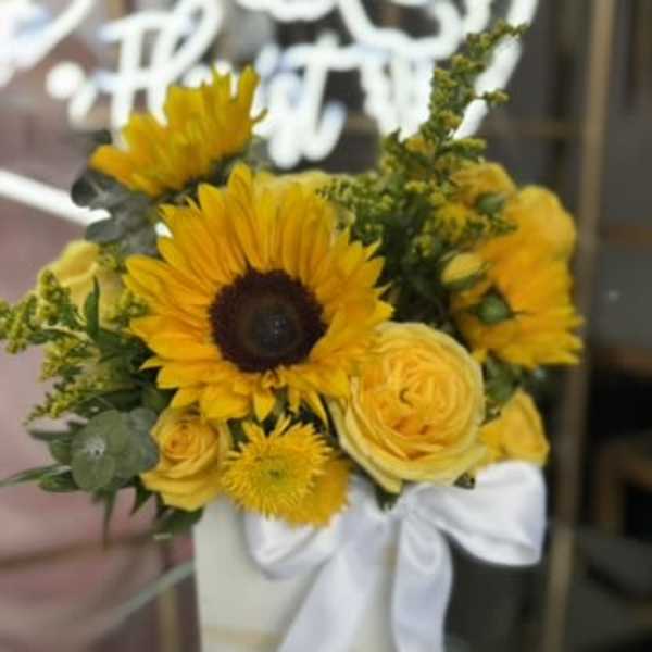 Yellow sunflower and rose bouquet in a white vase with a white ribbon