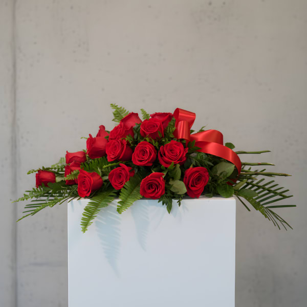 Red rose arrangement with a red ribbon on a white pedestal