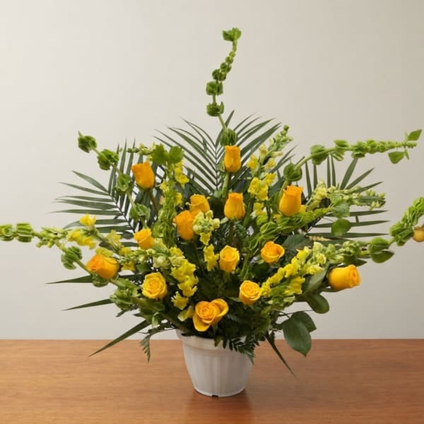Yellow roses and snapdragons arranged in a white pot