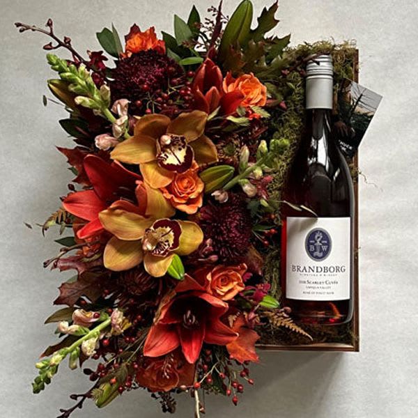 Autumn floral gift box with red and orange flowers beside a wine bottle