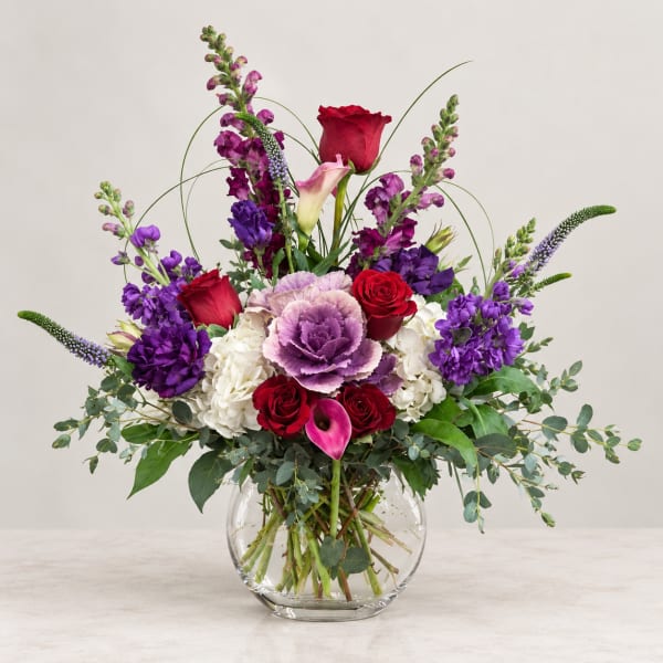 Mixed bouquet of red, purple, and white flowers in a clear glass vase