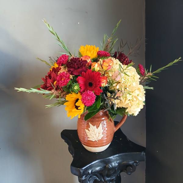 Mixed bouquet in a brown ceramic pitcher with yellow, pink, red, and cream blooms