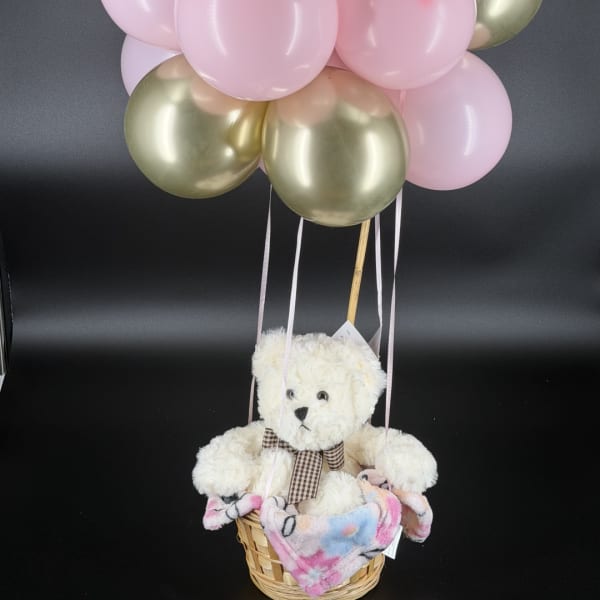 Teddy bear in a basket with pink and gold balloons above