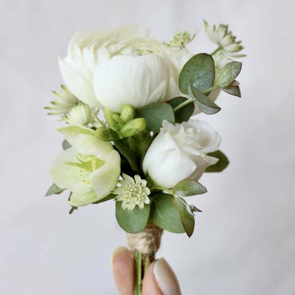 Small white floral boutonniere with green foliage held in a hand