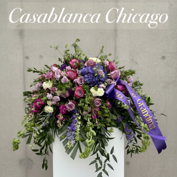 Large purple and pink floral arrangement in a white container with a ribbon