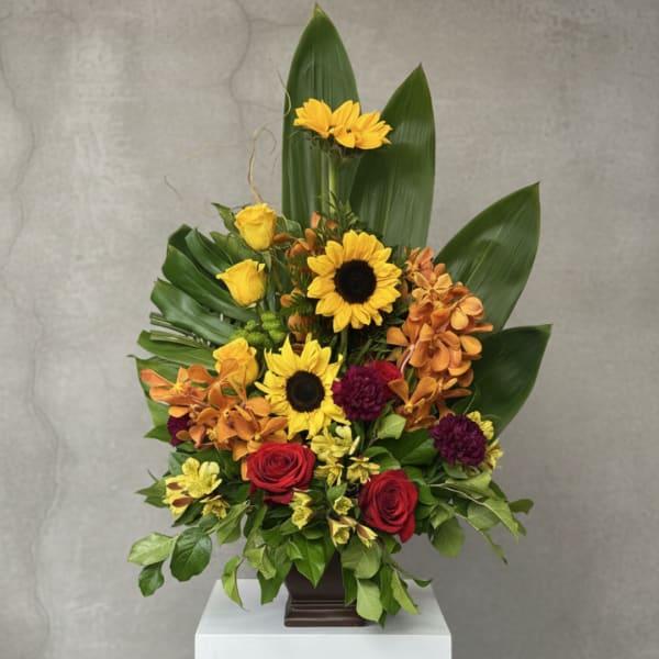 Mixed bouquet with sunflowers, red roses, and orange orchids in a dark vase
