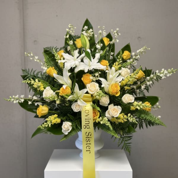 White lilies and yellow roses in a vase with a yellow ribbon