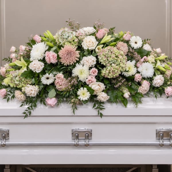 Pastel floral casket spray with roses, lilies, and white daisies