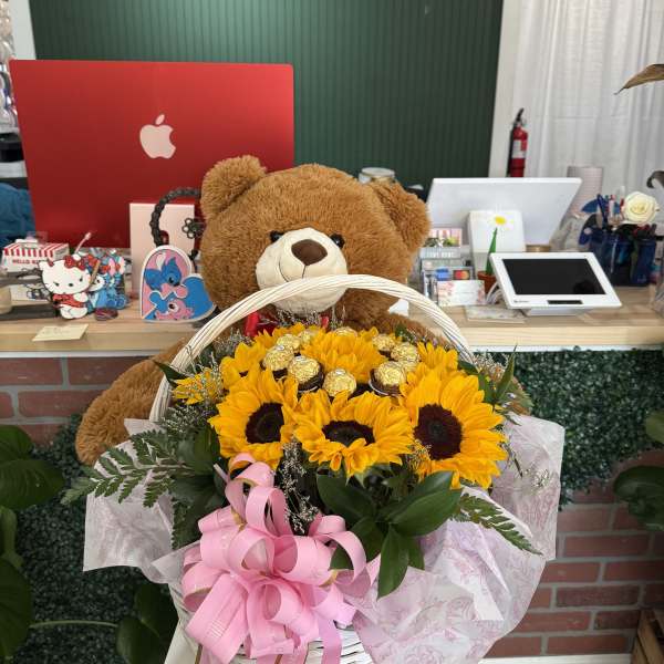 Basket of sunflowers with a teddy bear and pink ribbon