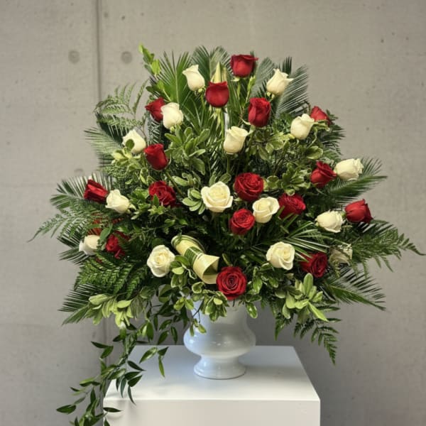 Red and white roses arranged in a white vase with lush greenery